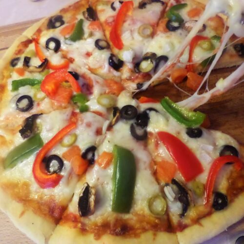 Homemade Italian pizza topped with colorful vegetables, melted mozzarella, and Parmesan, served on a rustic wooden plate