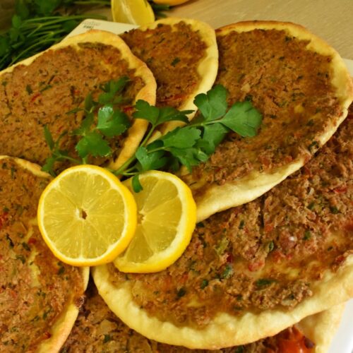 Homemade Lahmacun Turkish pizzas on a plate, topped with fresh parsley and served with lemon slices for garnish