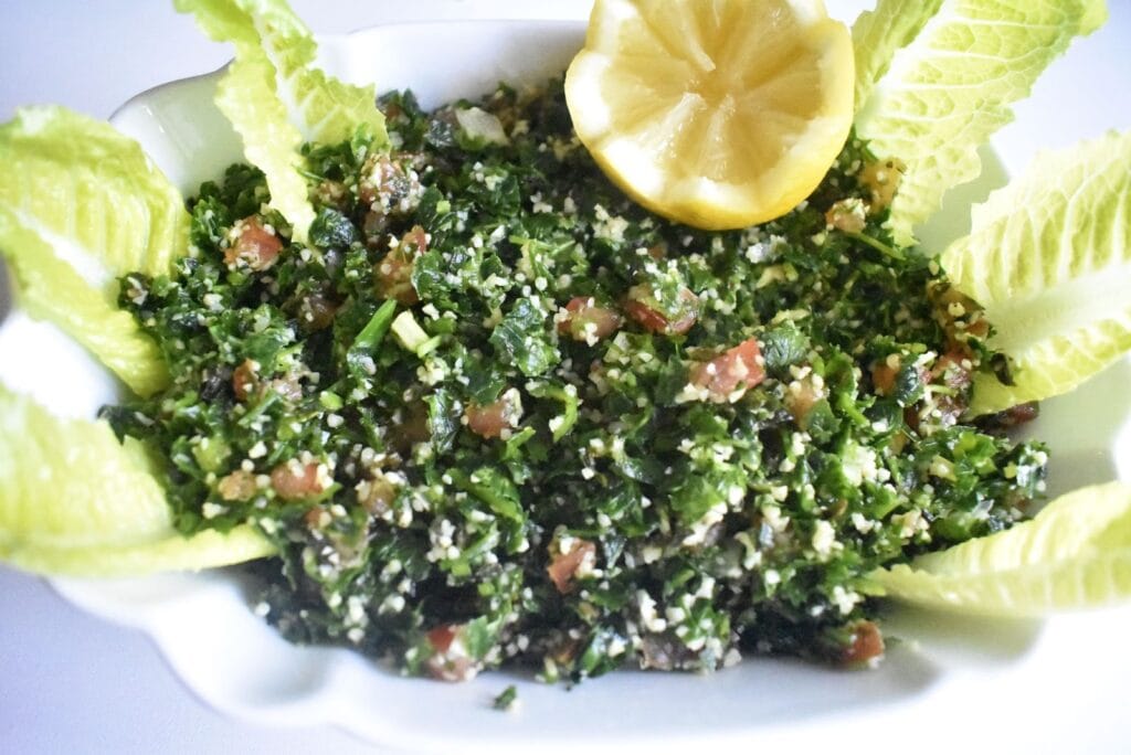 Fresh tabouli salad, mixed finely chopped parsley, tomato and bulgur in served in a white salad plate, decorate with a half lemon and baby lettuce leaves
