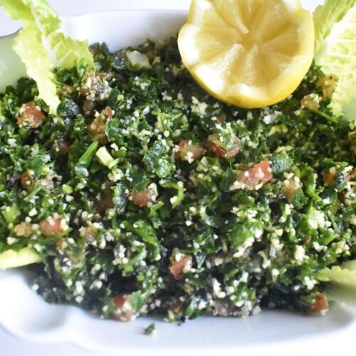 Fresh tabouli salad, mixed finely chopped parsley, tomato and bulgur in served in a white salad plate, decorate with a half lemon and baby lettuce leaves