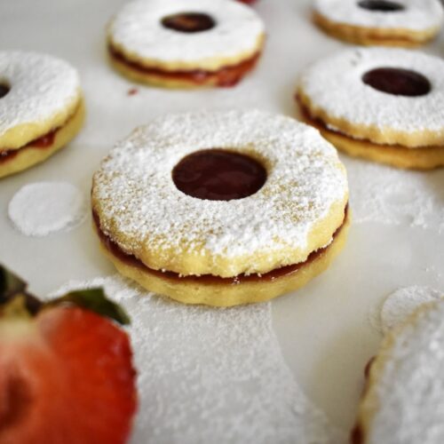 French Sable Cookies filled with a strawberry jam and covered with a powdered sugra with half strawberry around it cookies are on a parchment paper