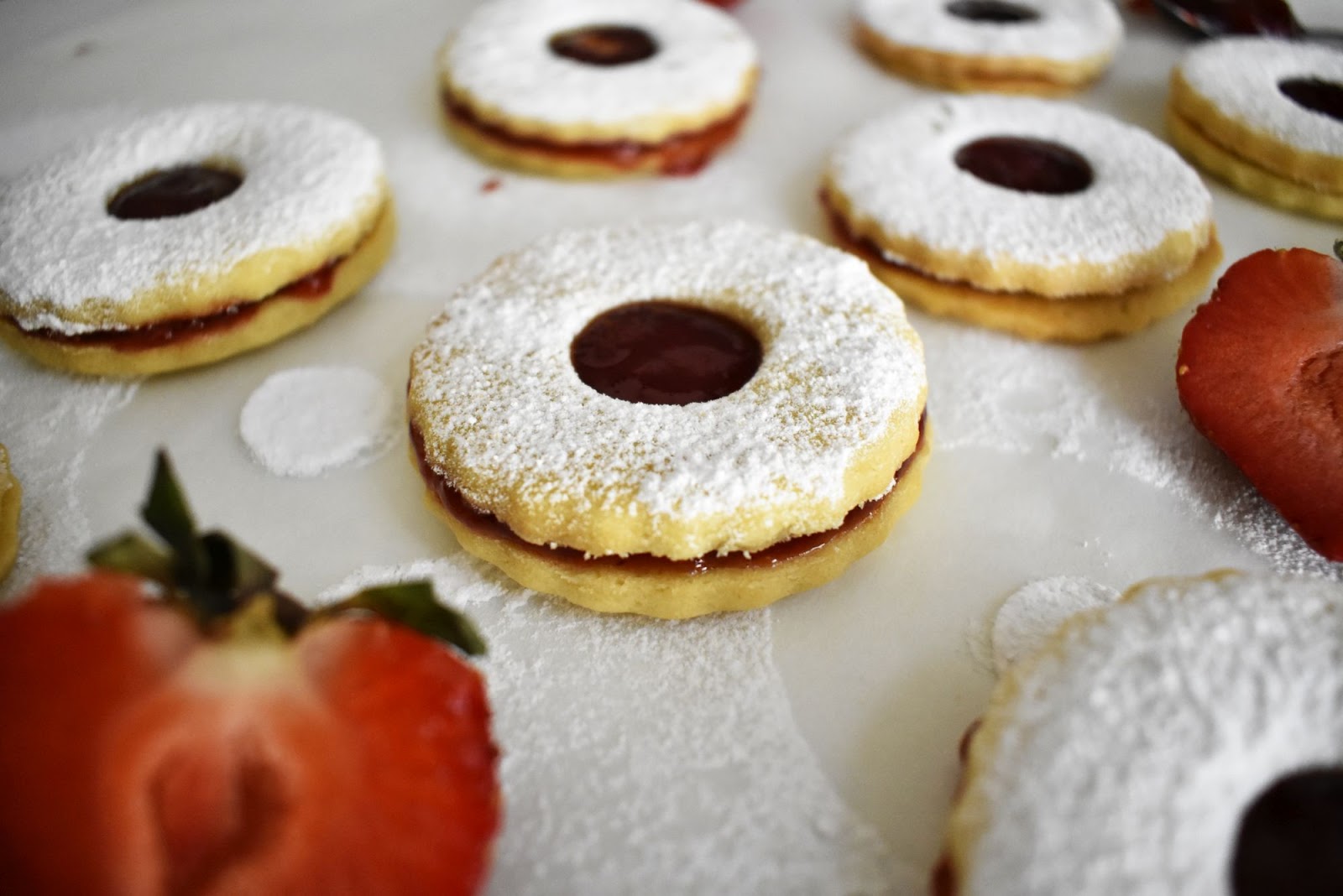 French Sable Cookies filled with a strawberry jam and covered with a powdered sugra with half strawberry around it cookies are on a parchment paper