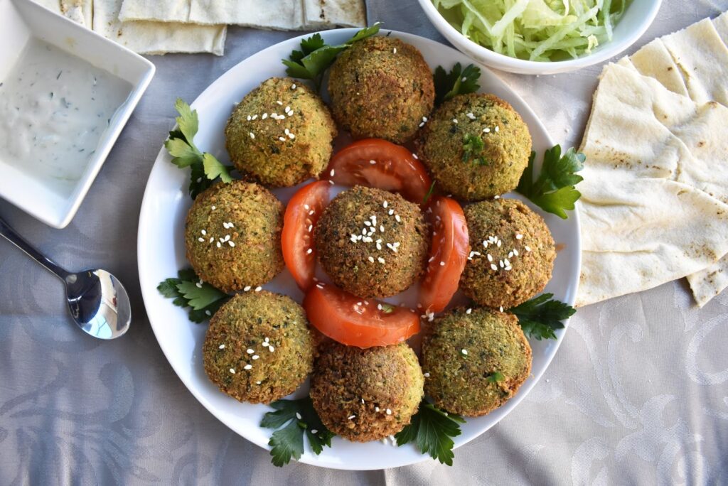 Crispy Homemade Middle Eastern falafel served on a round white plate, garnished with fresh tomato slices and parsley
