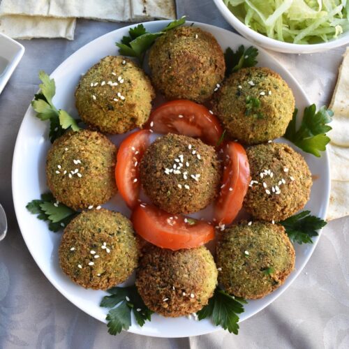 Crispy Homemade Middle Eastern falafel served on a round white plate, garnished with fresh tomato slices and parsley