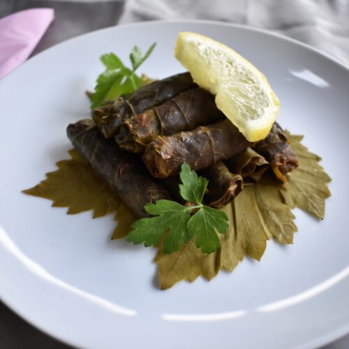 Stuffed grape leaves served on a white plate, garnished with a fresh lemon slice on top.