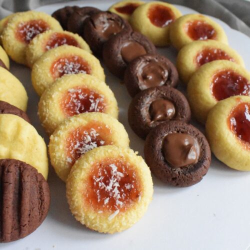 Tea chocolate and vanilla cookies, the vanilla cookies topped with a jam and the chocolate topped with nutella. Served in a white plate