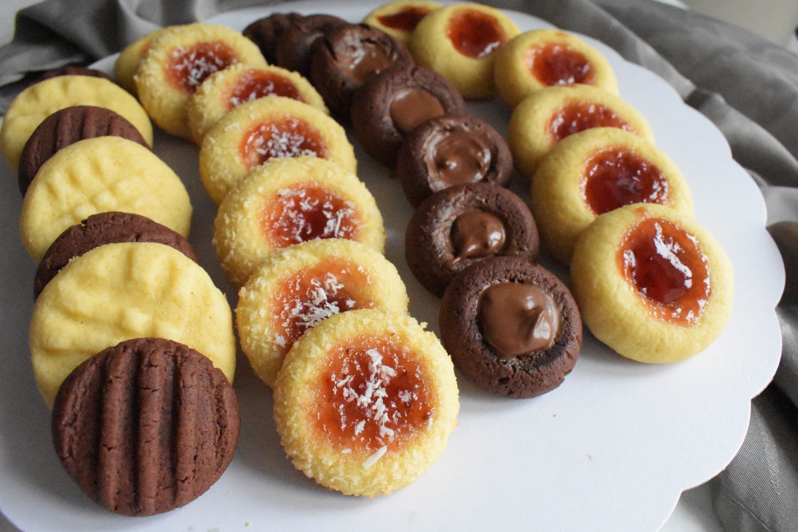Tea chocolate and vanilla cookies, the vanilla cookies topped with a jam and the chocolate topped with nutella. Served in a white plate