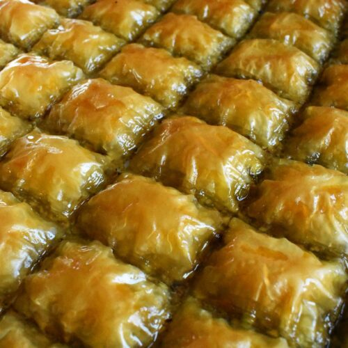 Homemade golden pistachio baklava squares arranged neatly in a baking tray, glistening with syrup