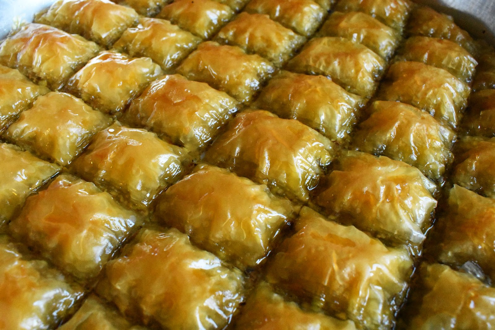 Homemade golden pistachio baklava squares arranged neatly in a baking tray, glistening with syrup