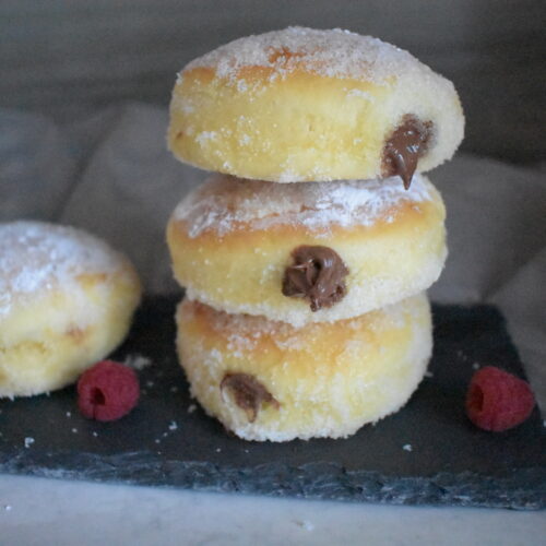 Baked Donuts Filled with Nutella served in a black plate and covered with powder sugar