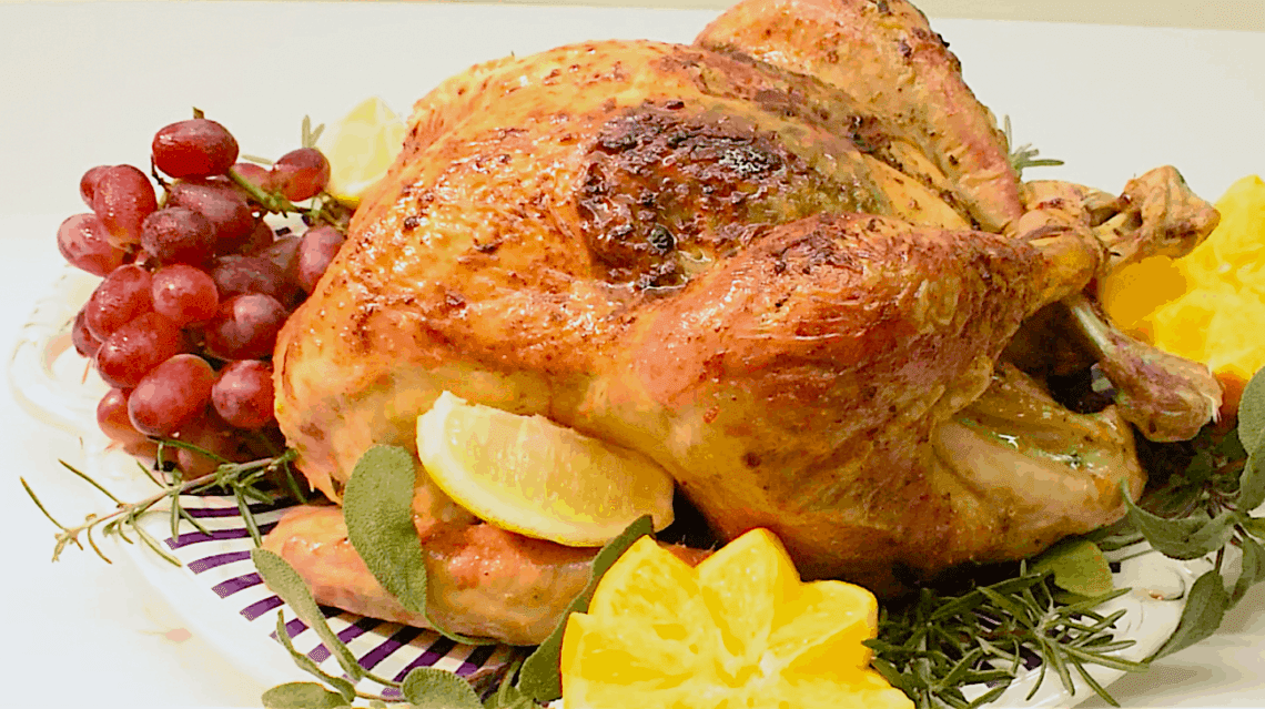 Golden brown Roast Turkey served with fresh herbs, lemon slices and red grapes around