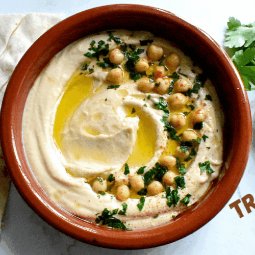 Creamy hummus served in a classic brown dish, surrounded by Lebanese bread.