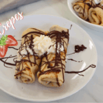 Classic French crepes served on a white plate, topped with whipped cream and drizzled with melted chocolate.