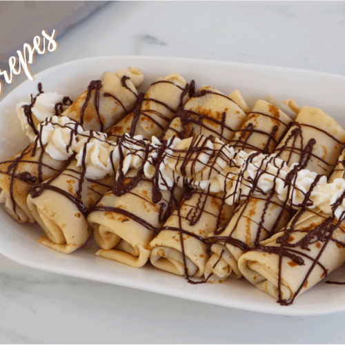 Classic French crepes served on a white plate, topped with whipped cream and drizzled with melted chocolate.