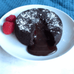 Molten chocolate lava cake served on a white plate with rich chocolate oozing out, garnished with two fresh raspberries.