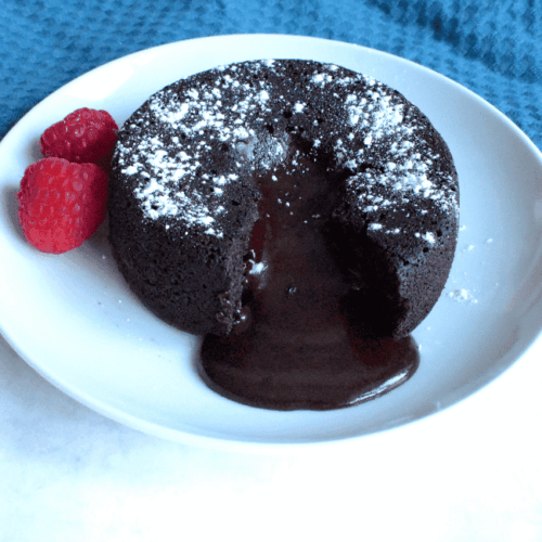 Molten chocolate lava cake served on a white plate with rich chocolate oozing out, garnished with two fresh raspberries.