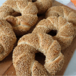 Six freshly baked Turkish simit bread rings coated with golden sesame seeds, served on rustic wooden plate