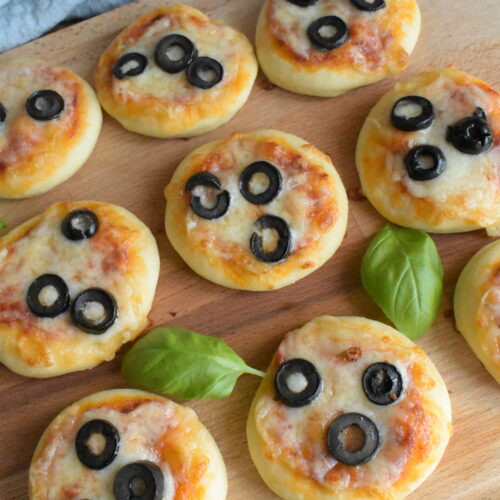 Mini pizzas served on a wooden board, topped with melted cheese and fresh black olive slices