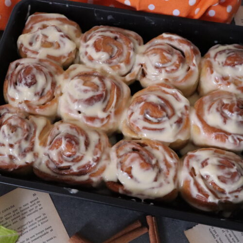 homemade cinnamon rolls served in a black tray and topped with cream cheese frosting