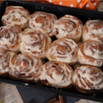 homemade cinnamon rolls served in a black tray and topped with cream cheese frosting